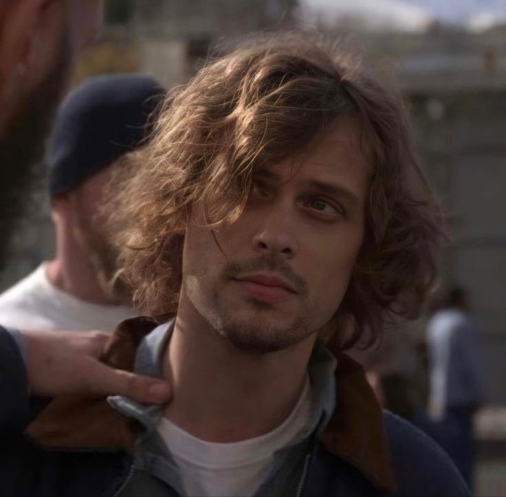 a man with long curly hair standing next to another man