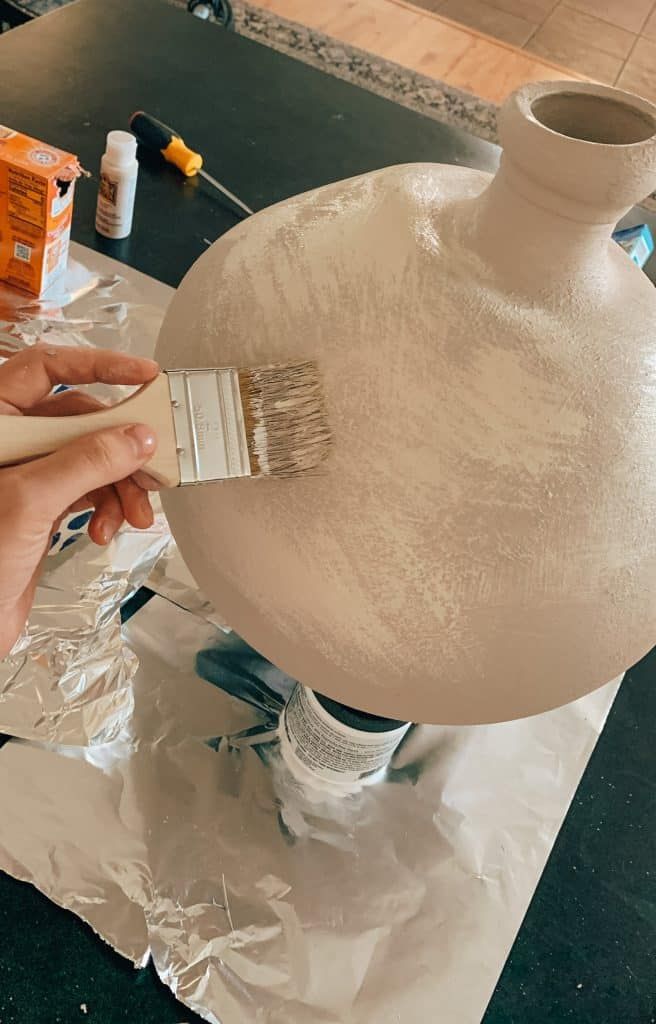 a person is painting a vase with white paint