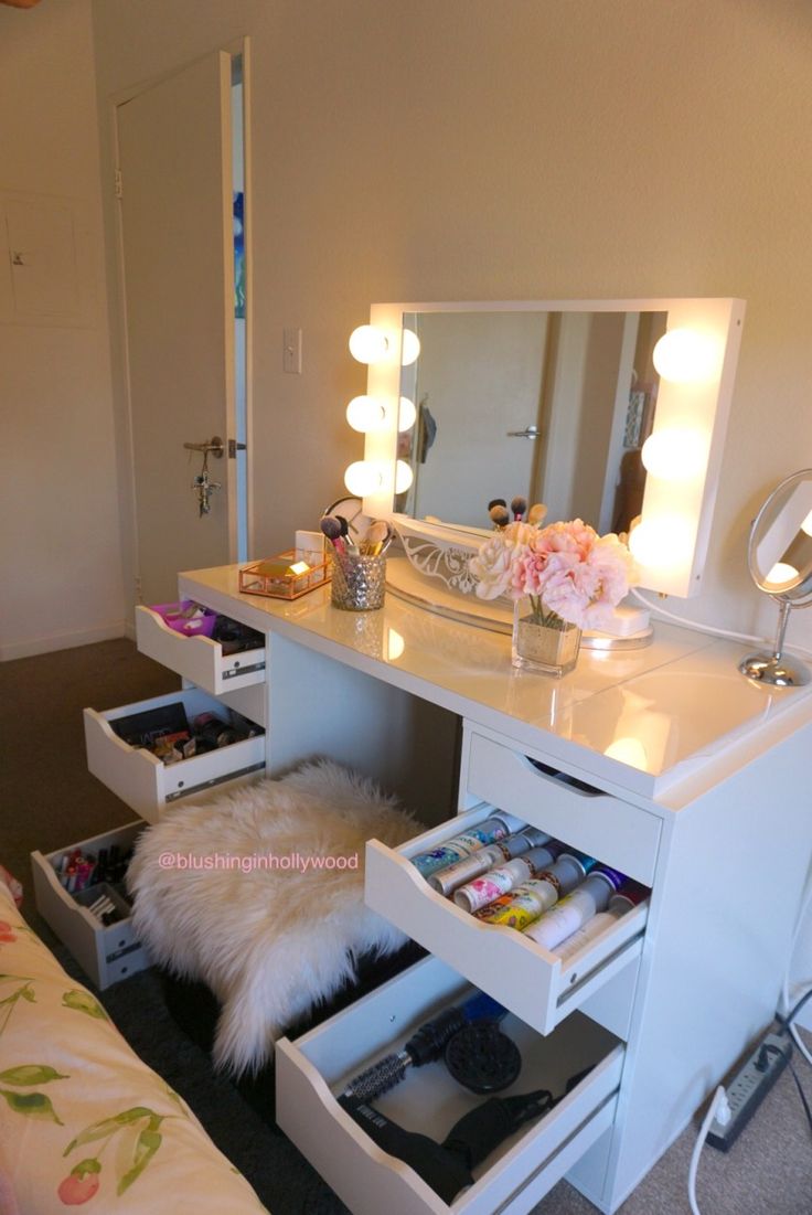 a white vanity table with drawers and lights on the mirror above it in a bedroom