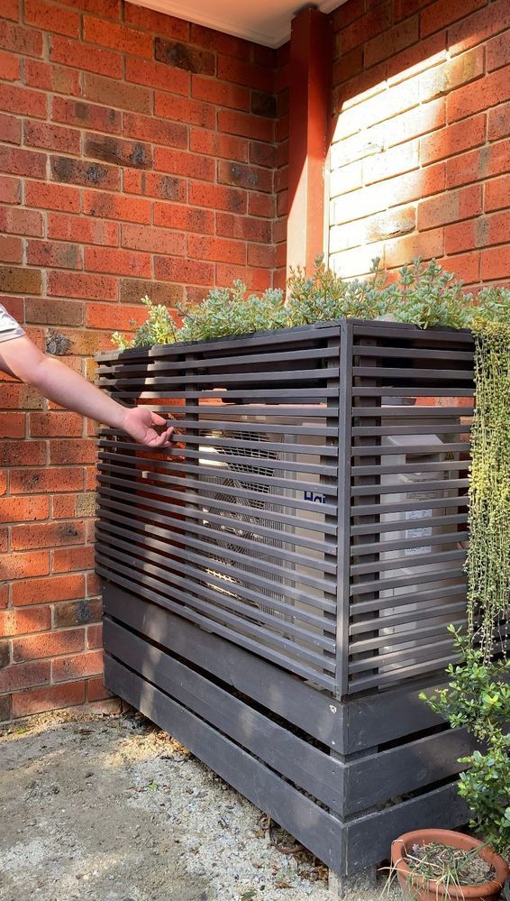 a person standing next to a planter on the side of a brick building with plants growing out of it