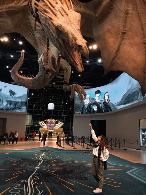 a woman standing in front of a giant fake dragon on display at a museum with people watching