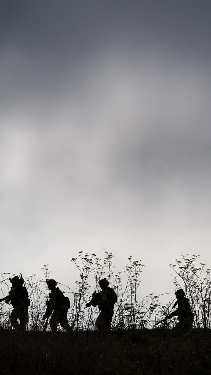 silhouettes of soldiers walking up a hill against a cloudy sky