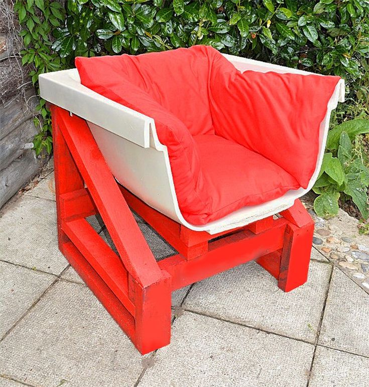 a red and white chair sitting on top of a cement floor next to a bush