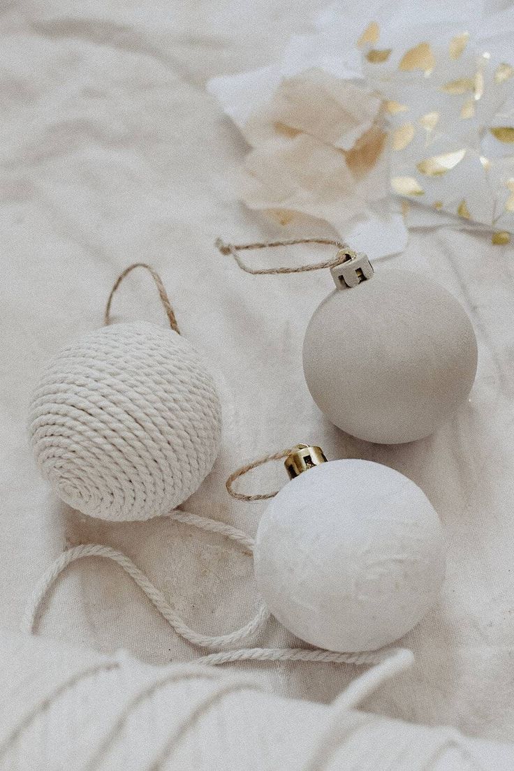 three white balls are sitting on a bed next to some twine and gold ornaments