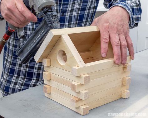 a man holding a hammer next to a small wooden house on top of a table