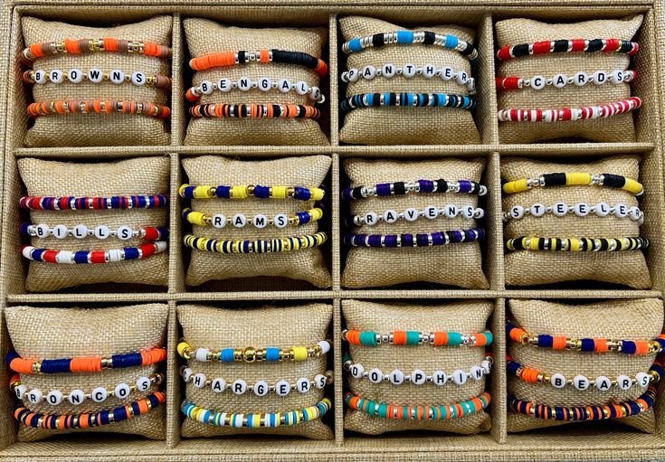 a box filled with lots of colorful bracelets on top of a wooden table next to pillows