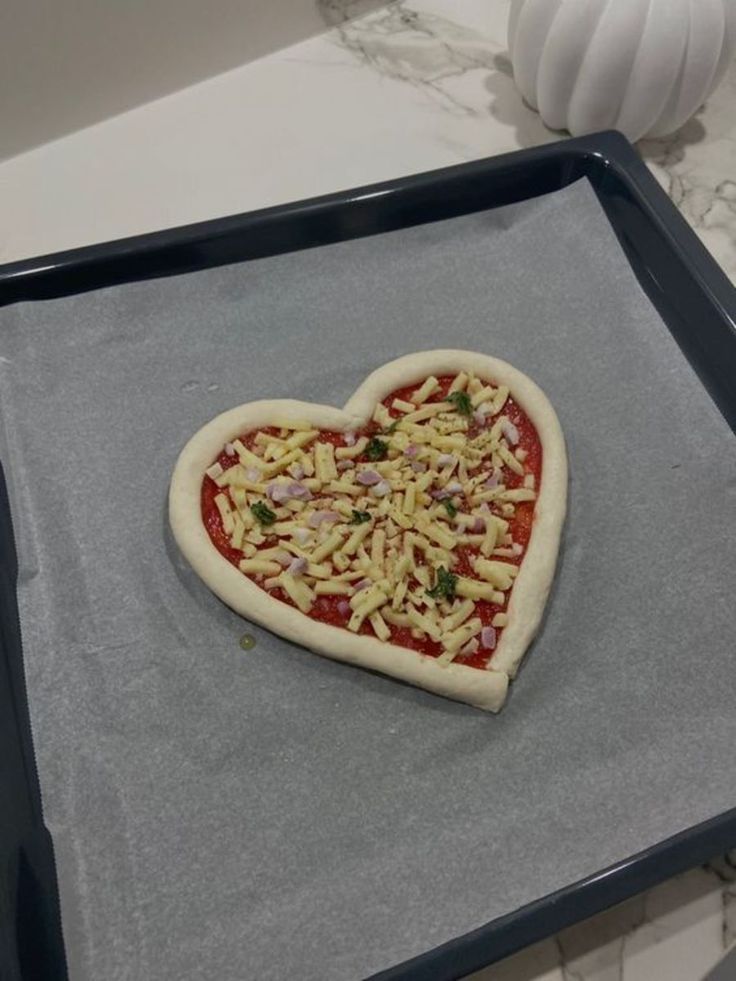 a heart shaped pizza sitting on top of a cookie sheet covered in cheese and toppings