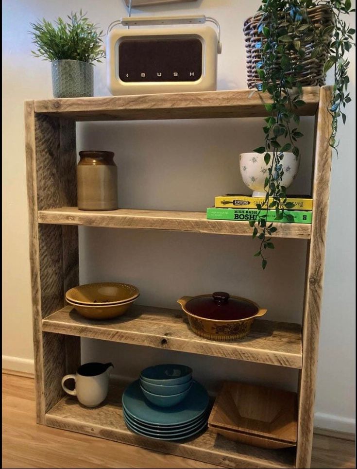 a wooden shelf with plates and bowls on it in front of a microwave, potted plant and other kitchen items