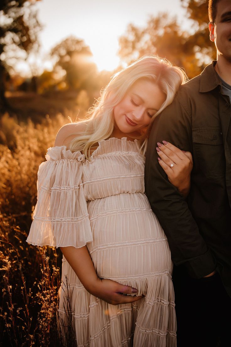 a pregnant woman standing next to a man in a field with the sun behind her