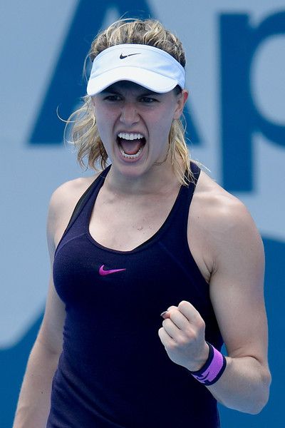 a woman holding a tennis racquet in her right hand and yelling at the camera