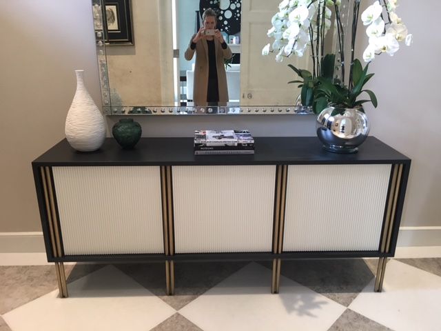 a black and white sideboard with vases on it in front of a mirror