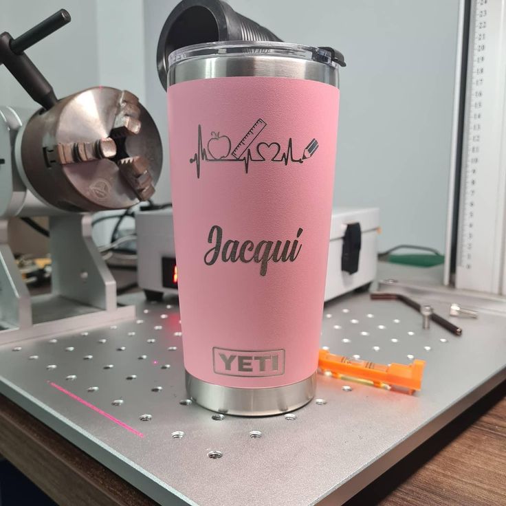 a pink yeti coffee cup sitting on top of a metal table next to a grinder