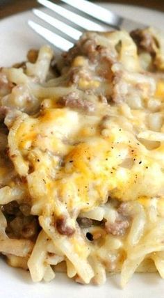 a white plate topped with macaroni and cheese covered in ground beef next to a fork