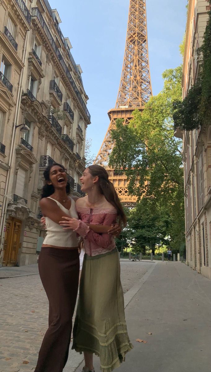 two women standing next to each other in front of the eiffel tower