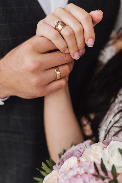 a couple holding hands with wedding rings on their fingers and flowers in front of them