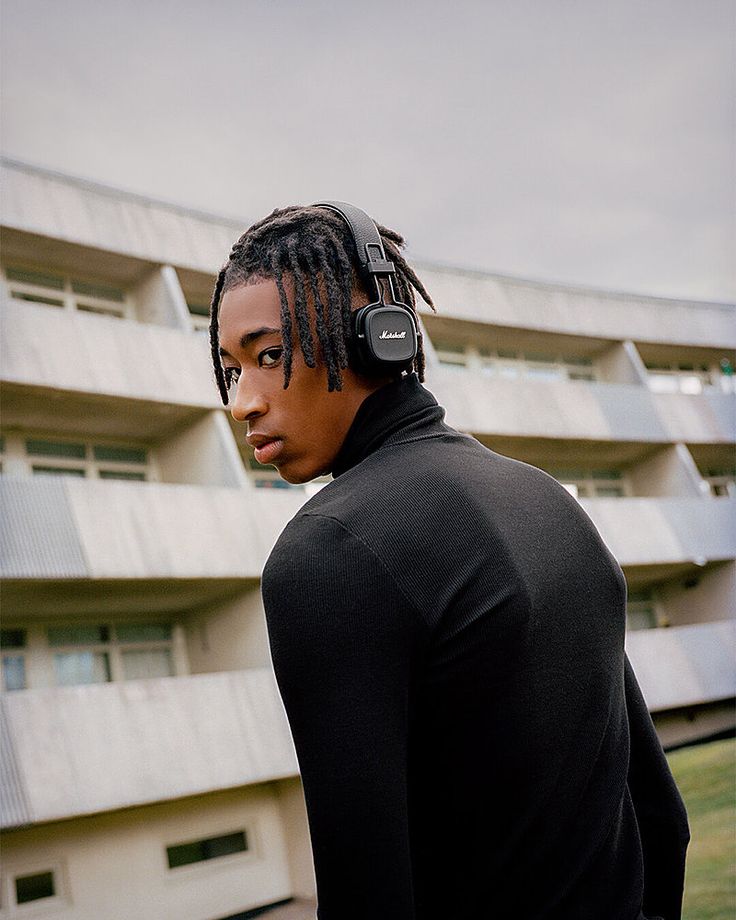 a man with dreadlocks standing in front of an apartment building wearing headphones