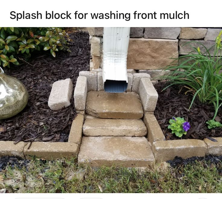 an outdoor toilet in the middle of some grass and flowers next to a rock wall