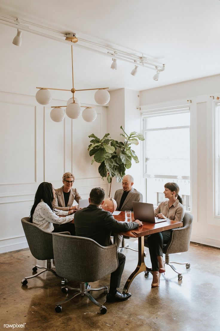 five people sitting around a table with laptops