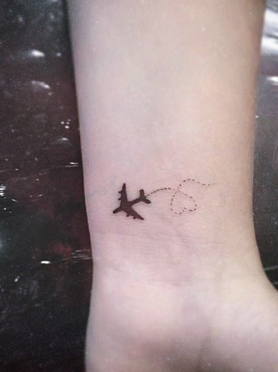 a small airplane tattoo on the wrist is shown in black and grey ink, with dots running across it