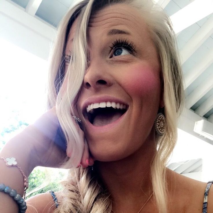 a woman with blonde hair smiling and holding her hand up to her face while wearing jewelry