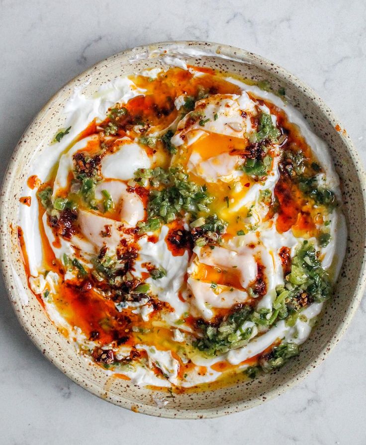 a white bowl filled with food sitting on top of a marble countertop next to a knife and fork