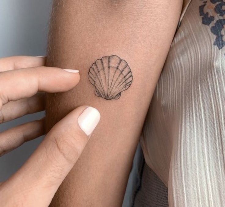 a woman's arm with a shell tattoo on the left side of her arm