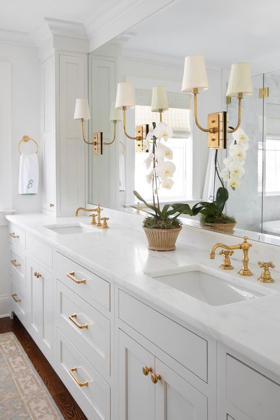 a white bathroom with two sinks and gold faucets