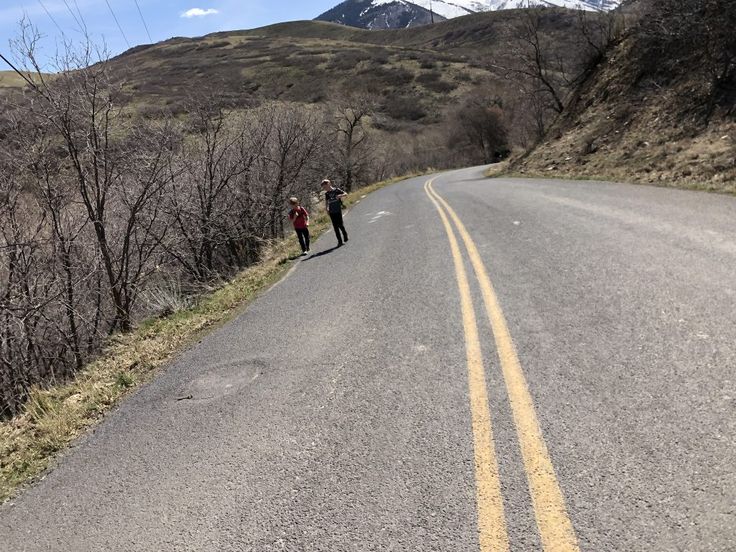 two people standing on the side of a road with mountains in the backgroud