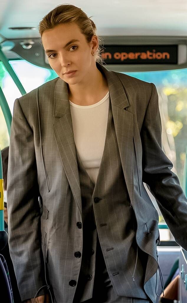 a woman in a suit and white shirt standing on a bus with her hands in her pockets