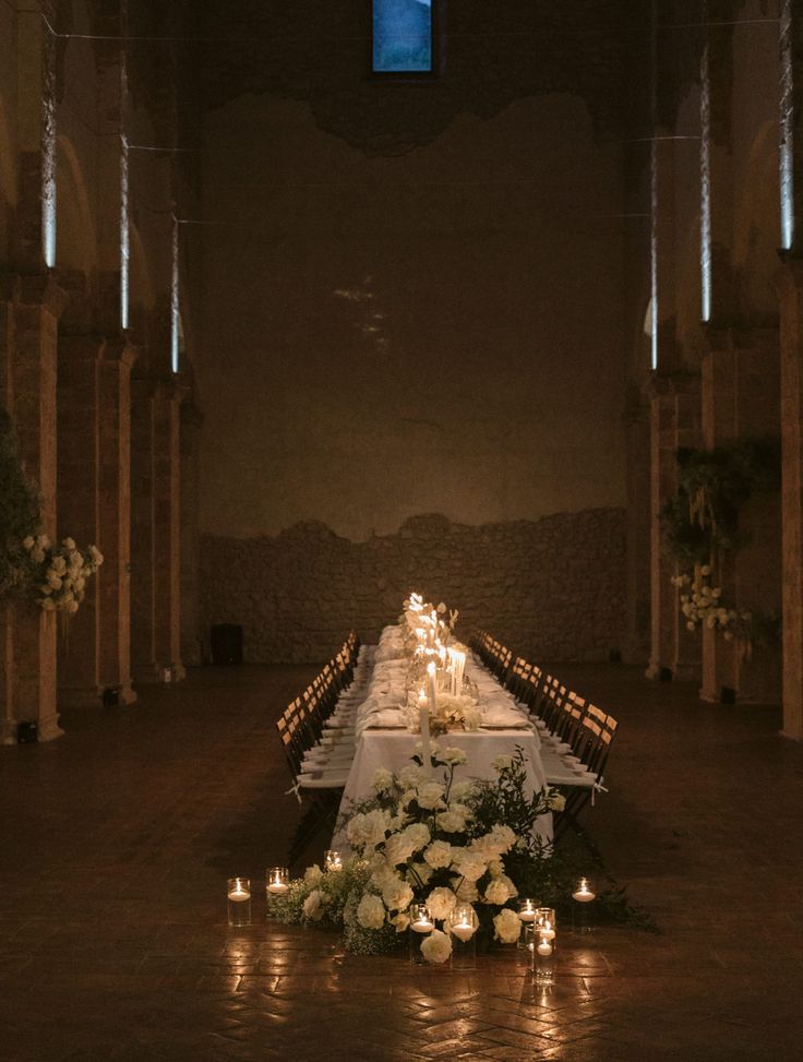 a long table with candles and flowers on it in the middle of an empty room