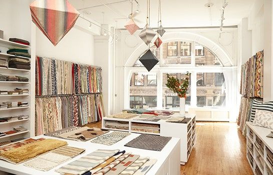 a room filled with lots of different types of fabrics and rugs on shelves next to windows