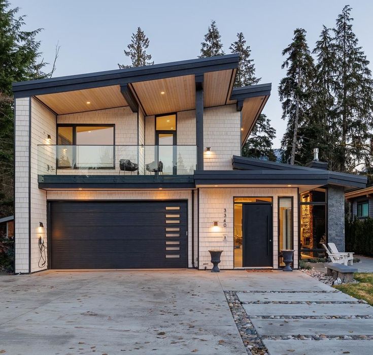 a modern house with two garages and an attached deck on the top floor, surrounded by trees