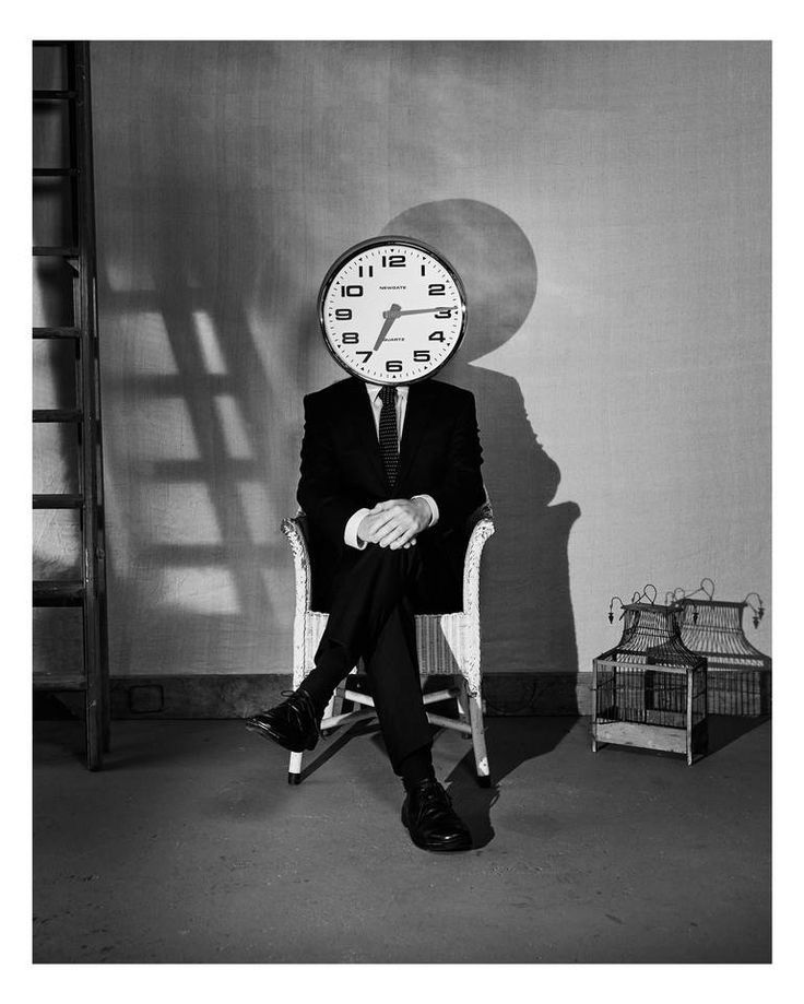 a man sitting in a chair with a clock on his head over his face and legs