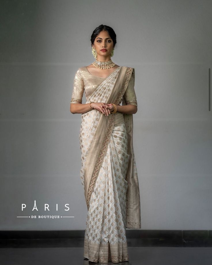 a woman in a white and gold sari is posing for the camera with her hands on her hips