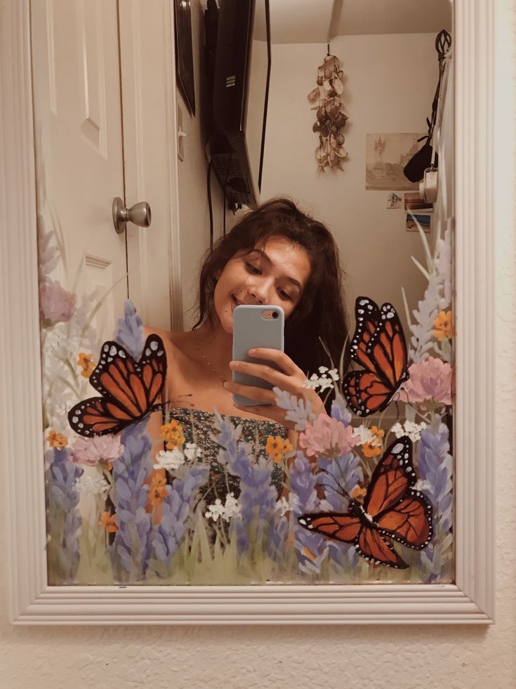 a woman taking a selfie in front of a mirror with butterflies on the wall