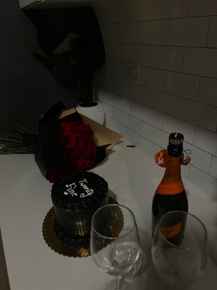 a bottle of champagne and two wine glasses on a counter with a cake in the background