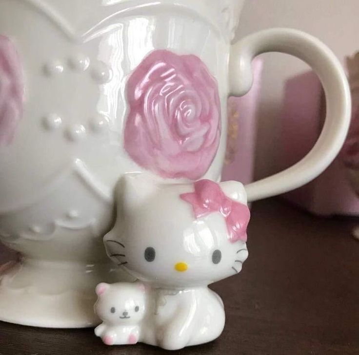 a hello kitty figurine sitting next to a coffee cup with a pink rose on it