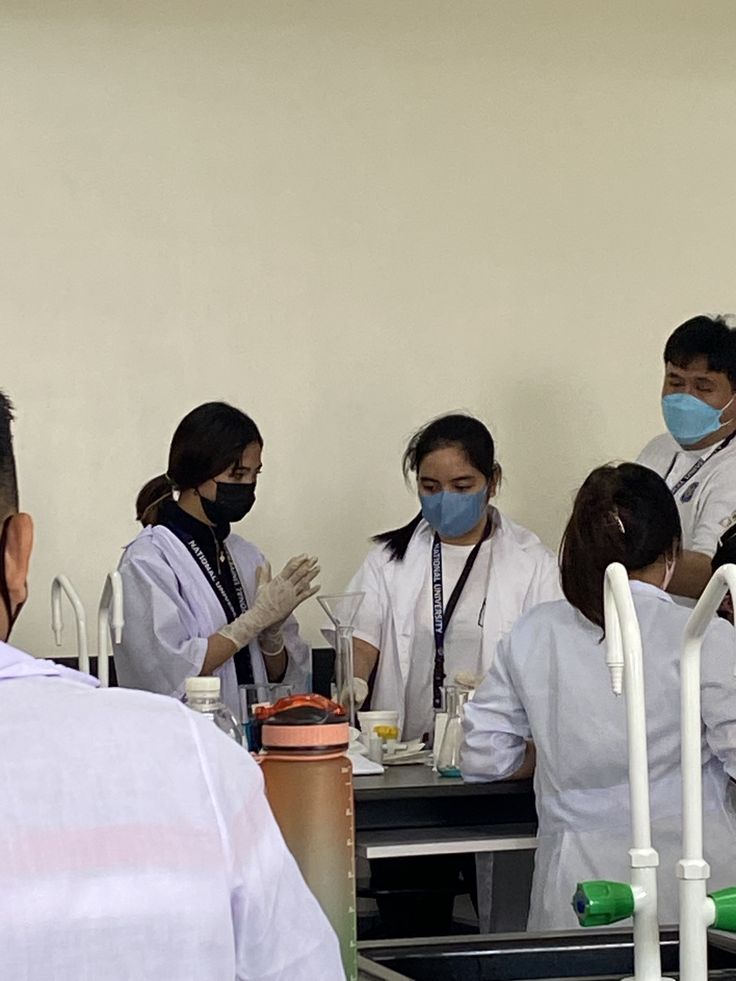 several people in white lab coats and face masks are standing around a table with medical supplies