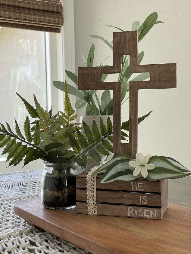 a wooden cross sitting on top of a table next to a vase filled with plants