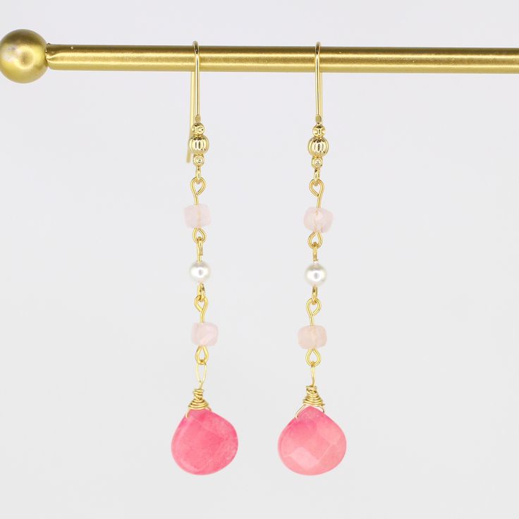 These elegant hand-wired earrings showcase a classic drop design adorned with two pink Jade gemstones, four pale pink Morganite stones, and two luxurious South Sea Pearls. With a 3.25" drop and crafted from gold-plated metal, they add a refined touch to any look. Pink Jade is believed to promote love, reduce stress, and bring luck, while pink Morganite is believed to foster joy and emotional calm. South Sea Pearls are thought to enhance clarity, aid self-expression, and boost self-esteem, making Pink Rose Quartz Wire Wrapped Jewelry, Pink 14k Gold Filled Dangle Jewelry, Elegant Pink Long Drop Earrings, Pink Pearl Drop Chandelier Earrings, Pink Rose Quartz Jewelry With Ear Wire, Pink Wire Wrapped 14k Gold-filled Jewelry, Pink Crystal Dangle Earrings With Ear Wire, Pink Rose Quartz Jewelry With Matching Earrings, Handmade Pink 14k Gold-filled Earrings