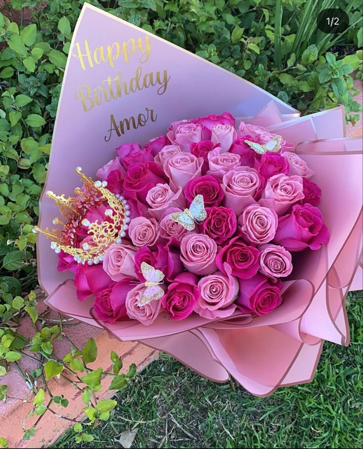 a bouquet of pink roses with a tiara on it sitting in front of some bushes