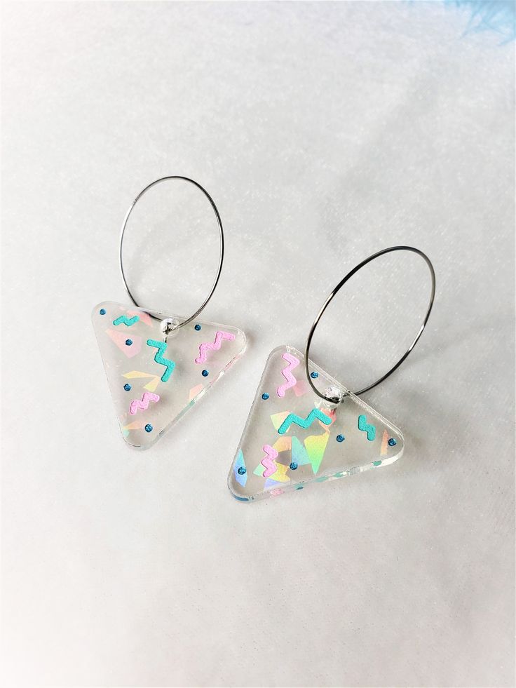 Rainbow Triangle 80s Holiday Party Hoop Earrings The hoops are made of stainless steel, they are about 1.25 inches acrossApproximately 1.25" wide, and 2.25" long from top of metal hoopThese are super fun and colorful earrings. Bright and cheery! With the lovely pastels and retro vibes, these earrings should give a good mood booster. They are made with a clear acrylic that feature rainbow iridescent shards of glitter, that shines differently depending on the light. The engraved details are hand p Playful Pink Hoop Earrings Gift, Colorful Hoop Earrings For Party, Pink Playful Handmade Hoop Earrings, Multicolor Modern Small Hoop Earrings, Playful Multicolor Hoop Jewelry, Modern Multicolor Small Hoop Earrings, Multicolor Fun Hoop Earrings For Party, Fun Multicolor Hoop Earrings For Party, Trendy Colorful Party Hoop Earrings