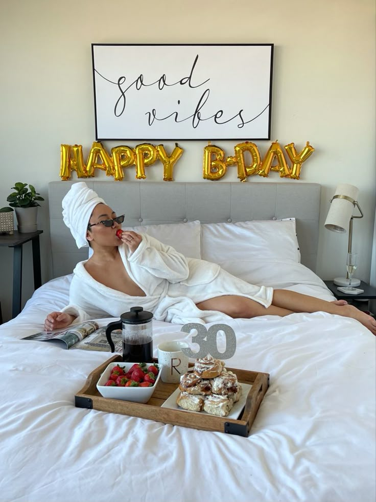 a woman laying in bed with food and drinks on the trays next to her