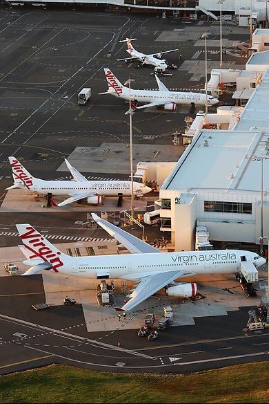 an aerial view of several airplanes parked at the airport terminal, including one for virgin australia