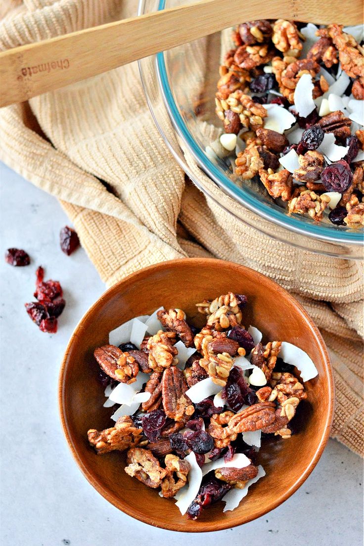 a bowl filled with nuts and cranberries next to a wooden spoon