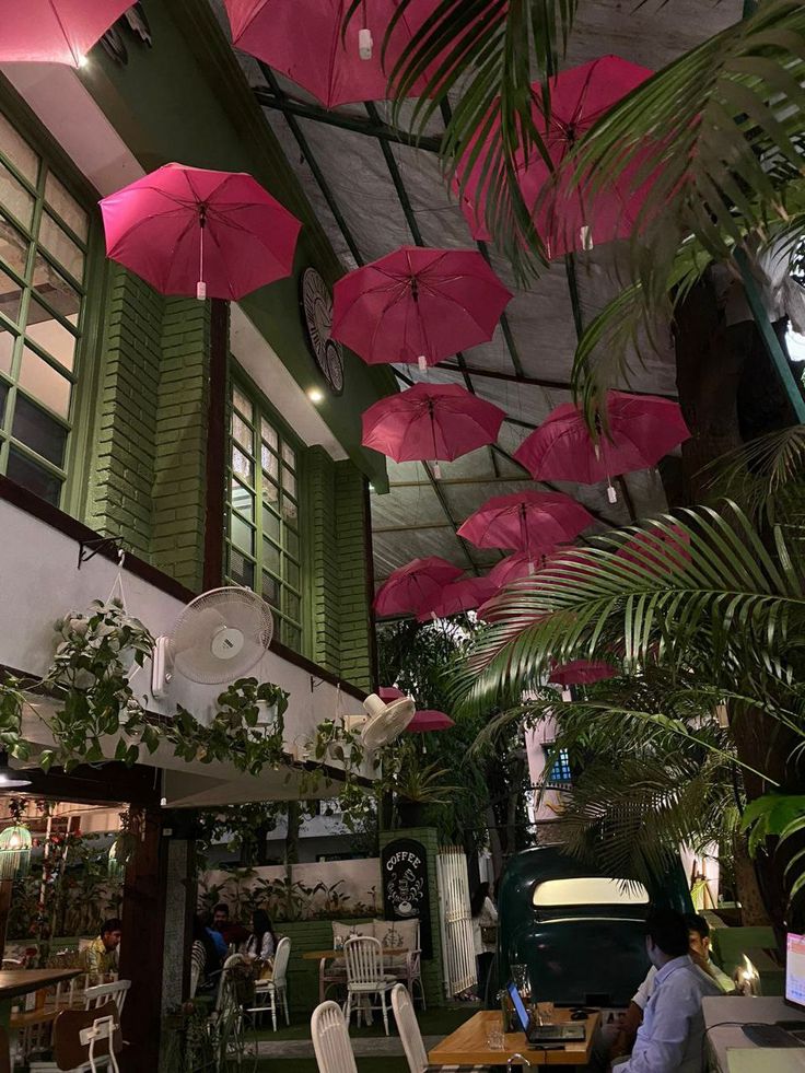 several pink umbrellas hanging from the ceiling in a room with green plants and tables