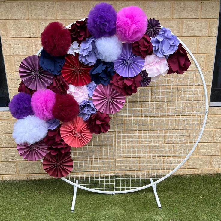 a wreath made out of paper flowers sitting on top of a white wire rack in front of a brick wall