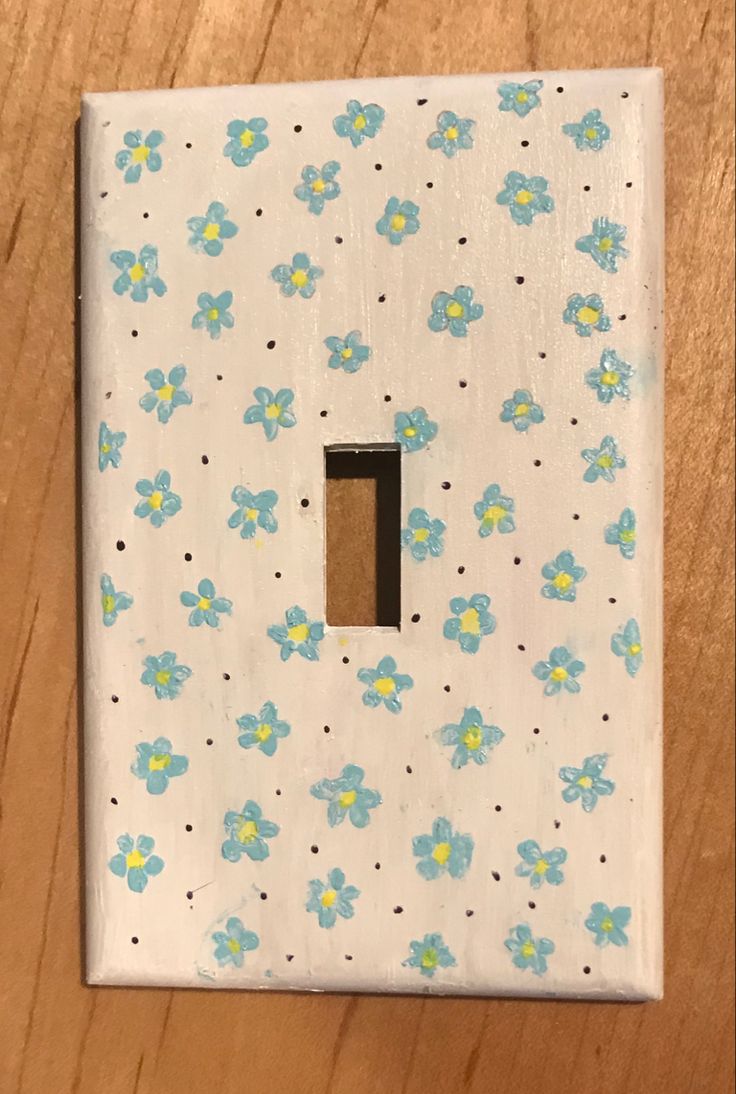 a white and blue flowered light switch plate on a wooden surface with a black hole in the middle