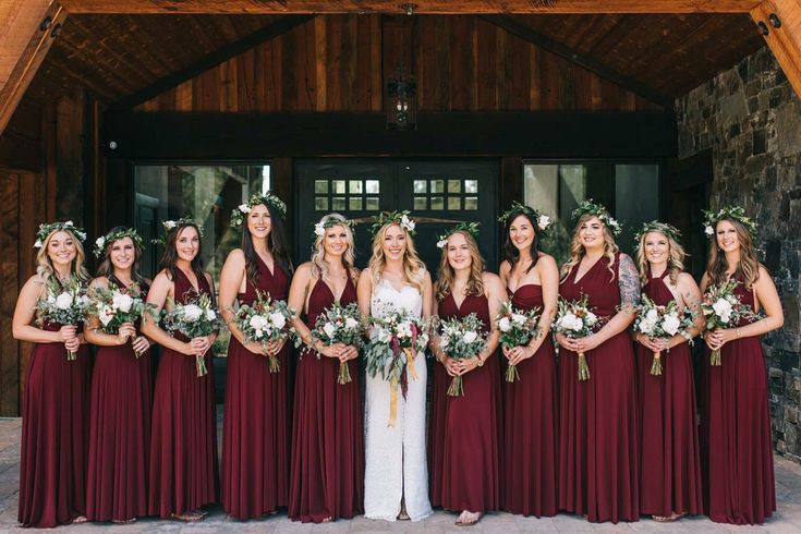 a group of women standing next to each other in front of a wooden building holding bouquets