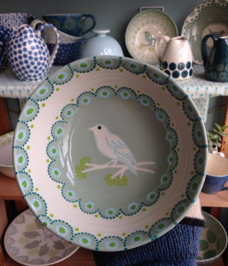 a plate with a bird painted on it in front of other plates and vases